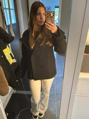 Svart design by si kappa - Snygg svart kappa med dubbelknäppning och bred krage. Klassisk modell som slutar vid höften och har en stilren look. Perfekt för dig som vill ha en enkel men trendig jacka till höst och vinter. Använd men i ett jätte bra skick utan defekter! 