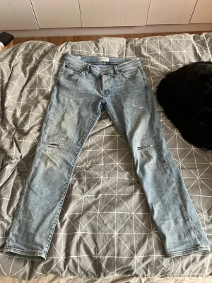 Ljusblå slitna jeans med raka ben  - Säljer ett par ljusblå jeans med raka ben och slitningar på båda knäna från Jack Jones Jeansen har klassisk femficksmodell och är tillverkade i denim. Perfekta för en avslappnad och trendig look.