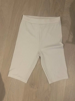 Vita ribbade cykelshorts - Säljer ett par vita ribbade cykelshorts med hög midja. De är stretchiga och har en enkel, clean look som passar perfekt till sommaren. Materialet känns mjukt och bekvämt mot huden. Knappt använda.