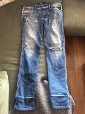 Blå slitna jeans med hål - Säljer ett par blå jeans från G-Star RAW med slitningar och hål på framsidan. Jeansen har en klassisk femficksmodell och raka ben. Snyggt tvättade detaljer och coolt sliten look, perfekt för dig som gillar streetstyle. W32 L32