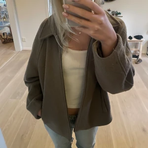 Khaki / grön ulljacka med dragkedja - Säljer en jacka i ullmaterial med dragkedja framtill och bred krage. Jackan har en avslappnad passform och två fickor på sidorna. Perfekt för dig som vill ha en stilren och enkel look till vardags. Den har gått sönder på insidan men det är inget som syns när man har på sig den. 
