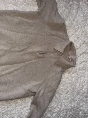 Beige halvzip tröja med krage - Snygg beige tröja med halvzip och klassisk krage. Tröjan har långa ärmar och ribbade muddar vid ärmslut och nederkant. Perfekt för lager på lager och enkel att matcha med olika outfits.