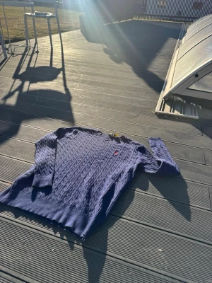 Blå kabelstickad tröja Polo Ralph Lauren - Snygg blå kabelstickad tröja från Polo Ralph Lauren med klassisk röd logga broderad på bröstet. Tröjan har rund halsringning, långa ärmar och ribbade muddar. Perfekt för dig som gillar stilrena och tidlösa plagg.