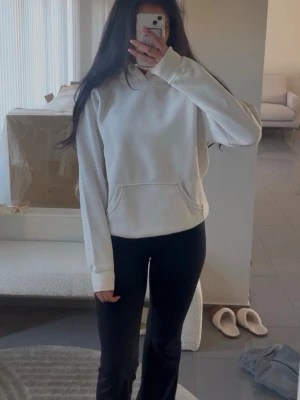 Vit hoodie  - Säljer en enkel och stilren vit hoodie med huva och stor magficka framtill. Hoodien har långa ärmar och ribbade muddar vid ärmslut och nederkant. Perfekt för en avslappnad och bekväm look.