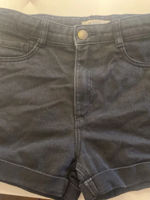 Svarta shorts med fickor - Snygga svarta shorts med uppvikta benslut. Shortsen har knapp och dragkedja framtill samt två bakfickor. Perfekta för varma dagar och enkla att matcha med olika stilar.