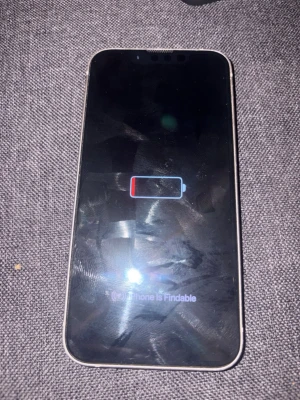 Vit iPhone med dubbla kameror - Säljer en vit iPhone med stilren design och rundade hörn. Baksidan är i glas och har två stora kameralinser samt Apples logga i mitten. Telefonen har en modern look och passar perfekt för dig som gillar snygg teknik. Liten sprick på kameran men inget som stör själva kameran funkar felfritt och en liten mindre spricka på kanten av telefonen