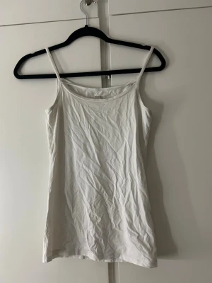 Vit linnetopp med smala axelband - En enkel och stilren vit linnetopp från H&M med smala axelband och rak passform. Perfekt att bära som lager eller till jeans och kjol. Tillverkad i mjuk bomull för en bekväm känsla.