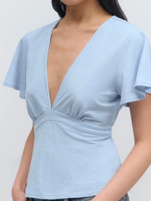 Ljusblå omlottopp med knyt ifrån Gina tricot  - Snygg ljusblå omlottopp med djup v-ringning och korta, vida ärmar. Toppen har ett markerat midjeband och knyt i ryggen för en feminin siluett. Tillverkad i mjuk bomull som känns skön mot huden.