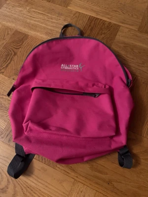 Rosa ryggsäck All Star Gymnastics - Ord pris: 600:- Snygg rosa ryggsäck från All Star Gymnastics med ett stort huvudfack och en praktisk ytterficka med dragkedja. Justerbara axelband och bärhandtag upptill. Tillverkad i slitstark textil, perfekt för träning eller skola.
