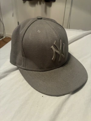 Grå New Era Yankees keps - Snygg grå keps från New Era med New York Yankees-logga broderad framtill i matchande ton. Klassisk rak skärm och sexpanelers design. Tillverkad i bomullstyg och har ventilerande hål upptill för extra komfort.