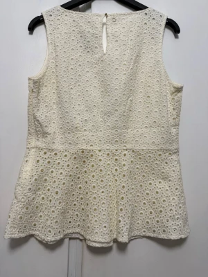 Vit ärmlös blus med spetsdetaljer från Stockholm  - Söt vit blus i ärmlös modell med rund halsringning och vackra spetsdetaljer i cirkelmönster. Blusen har en lätt utsvängd passform och knapp i nacken. Perfekt för en fräsch och somrig look.