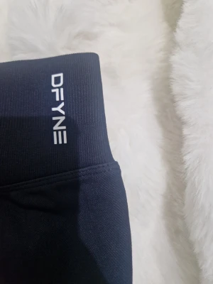 Svarta leggings från DFYNE - Säljer ett par svarta leggings från DFYNE med hög midja och stretchigt material. Diskret logga på linningen och texten 'LET NOBODY DFYNE YOU' på insidan. Perfekta för träning eller chill dagar.