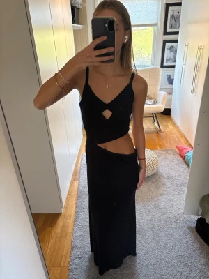 Svart långklänning med cut out - Svart långklänning med smala axelband och snygga cut out-detaljer vid midjan och bröstet. 