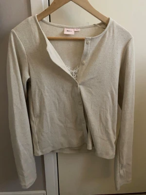 Beige ribbad kofta från gina - Säljer en beige ribbad kofta från Gina med rund halsringning och knäppning framtill. Koftan har långa ärmar och är tillverkad i ett mjukt, stretchigt material som sitter skönt på kroppen. Perfekt att slänga över ett linne eller t-shirt.