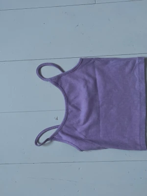 Ljuslila ribbad linnetopp - Säljer en ljuslila ribbad linnetopp med smala axelband. Toppen har en enkel och stilren design, perfekt att matcha med jeans eller kjol. Materialet är mjukt och stretchigt för en bekväm passform.