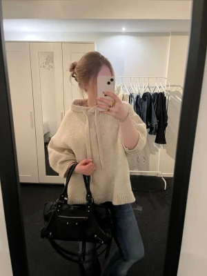 Beige stickad hoodie med luva - Mysig beige stickad hoodie med luva. Tröjan har en avslappnad passform, breda ärmar och ribbstickade muddar vid ärmslut och nederkant. Perfekt för lager-på-lager och chill dagar. Lite nopprig annars inga defekter, köpt från plick.