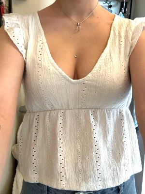 Vit broderad blus med volangärm - Söt vit blus med broderade detaljer och v-ringning. Toppen har volangärmar och är tillverkad i ett lätt bomullstyg med hålmönster.