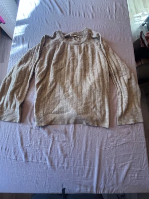 Beige stickad tröja med rund hals - Mysig beige stickad tröja med rund halsringning och långa ärmar. Tröjan har ribbstickade muddar vid ärmslut och nederkant samt en avslappnad passform. Perfekt för lager på lager och enkel att matcha med olika outfits.