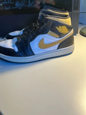 Nike Air Jordan 1 Mid svart/gul/vit - Snygga Nike Air Jordan 1 Mid sneakers i svart, vitt och gult läder. Klassisk siluett med gul swoosh och Air Jordan-logga på sidan. Skön passform och ikonisk design som alltid är trendig.priset kan diskuteras vid snabb affär 