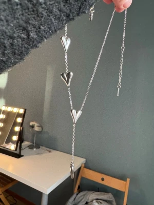 Silverfärgat halsband med hjärtan - Snyggt halsband i silverfärg med fyra större hjärtformade hängen längs en tunn kedja. Halsbandet har justerbar längd och hjärtana är i metall med en blank finish. Perfekt accessoar för att lyfta din outfit. Trendigt halsband!