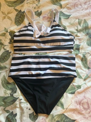 Randig bikini med rosett - Snygg bikini med svartvita ränder och en söt rosett framtill på toppen. Överdelen har justerbara axelband och hög midja på underdelen. Perfekt för strandhäng eller poolparty. Aldrig använd! 