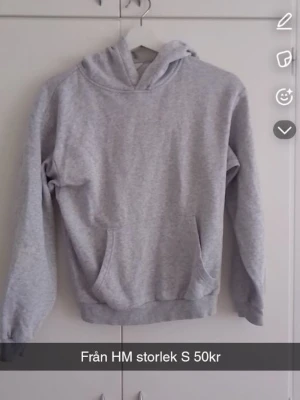 Grå hoodie från H&M med ficka - Klassisk ljusgrå hoodie från H&M med stor magficka och huva. Tillverkad i mjukt sweatshirtmaterial, perfekt för en avslappnad stil. Långa ärmar och ribbade muddar vid ärmslut och nederkant. Enkel och stilren design som passar till det mesta.