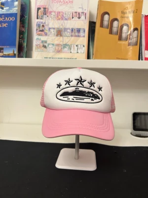 Rosa och vit truckerkeps med UFO-brodyr - Säljer en rosa och vit truckerkeps med mesh på sidorna och bak. Framtill finns en svart brodyr av ett UFO och fem stjärnor. Kepsen har böjd skärm och justerbar snapback. Perfekt för dig som vill sticka ut med en unik accessoar.