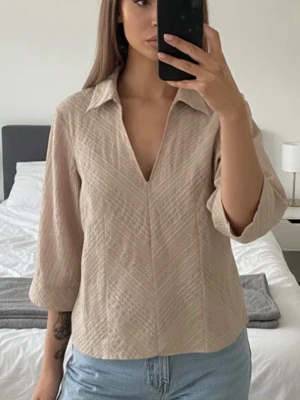 Beige skjortblus  med v-ringning - Snygg beige skjorta med v-ringning och diskret mönster. Skjortan har trekvartsärm och klassisk krage. Vintage från märket petite collection. Storlek 36 