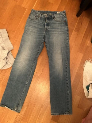 Blå raka jeans från Levi's - Klassiska blå jeans från Levi's med rak passform och fem fickor. Jeansen har en snygg tvättad look med ljusa partier på låren och knäna. Tillverkade i slitstarkt denimtyg och har traditionell knappgylf. Perfekta för en avslappnad stil.