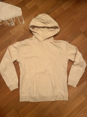 Beige hoodie  - Säljer en enkel och stilren beige hoodie med huva och stor magficka framtill. Hoodien har långa ärmar och ribbade muddar vid ärmslut och nederkant. Perfekt för en avslappnad och casual look.