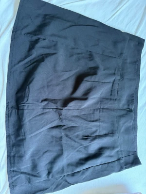 Svart kortkjol med dragkedja, shorts under  - En enkel och stilren svart kortkjol med diskret dragkedja i sidan. Kjolen har en rak passform och är tillverkad i ett mjukt tyg som känns bekvämt. Perfekt att matcha med olika toppar för en clean look.