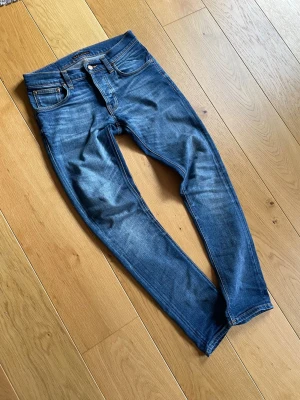 TVÄR FETA NUDIE GRIM TIM - Säljer ett par riktigt feta nudie jeans i modellen grim Tim! Jeansen har en snygg tvätt som passar året runt! Storlek 29/32 skriv vid frågor!