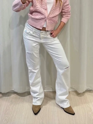 Vita low waist jeans med hål från Gina Tricot - Säljer ett par vita jeans från Gina Tricot med bootcut och slitna detaljer på låren och knäna. Klassisk femficksmodell med knapp och dragkedja framtill. Perfekta för en avslappnad och trendig look. Passar mig som är 165