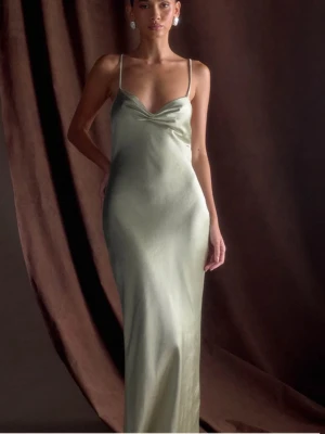 Ljusgrön balklänning  - Elegant ljusgrön långklänning med smala axelband och draperad v-ringning. Klänningen har en slank passform och är tillverkad i ett glansigt material som ger en lyxig känsla. Perfekt för dig som vill ha en stilren och modern look. Passar perfekt till balen eller bröllop. Aldrig använd. 