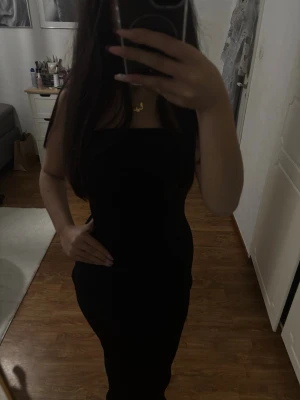 Svart axelbandslös långklänning - Säljer en elegant svart långklänning med axelbandslös design. Klänningen har en figurnära passform som framhäver siluetten och är perfekt för dig som gillar en stilren look. Materialet känns mjukt och följsamt mot kroppen.