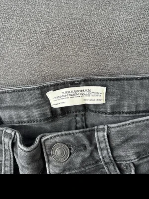 Gråa jeans från Zara Woman - Snygga grå jeans från Zara Woman Premium Denim Collection med slitna detaljer på bakfickorna. Klassisk femficksmodell och knappgylf. Jeansen har en tvättad look och är tillverkade i mjukt denimtyg som ger en avslappnad vibe.