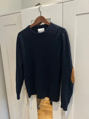 Mörkblå stickad tröja från Samsøe  - Mörkblå stickad tröja från Samsøe i ull och bruna mockadetaljer på armbågarna. Riktigt stilig och snygg😃 Extra nice med en skjorta under! Storlek S knappt använd. Skriv vid frågor! 