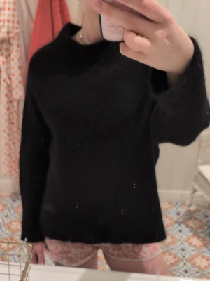 Svart stickad tröja med rund hals - En enkel och stilren svart stickad tröja med rund hals och långa ärmar. Tröjan har en rak passform och är perfekt för att matcha med olika outfits. Materialet ser ut att vara mjukt och mysigt, idealiskt för kyliga dagar.