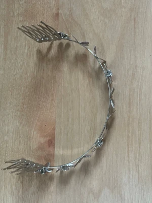 Silvrigt diadem med blommor och fjärilar - Säljer ett silvrigt diadem i metall med detaljerade blommor och fjärilar längs hela bågen. Diademet har kammar i ändarna för att sitta stadigt i håret och ger en elegant och unik look. Perfekt för dig som vill sticka ut med accessoarer med naturinspirerade detaljer.
