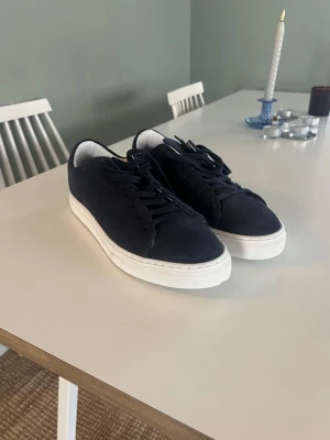 Mörkblåa sneakers med vit sula - Snygga mörkblå sneakers med ovandel i mocka och klassisk vit gummisula. Skorna har låga skaft och matchande mörkblå skosnören. Perfekta för en clean och stilren look.