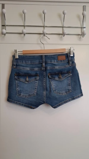 Blå denimshorts från Subdued - Snygga blå denimshorts från Subdued med dubbla silverknappar i midjan. Shortsen har bakfickor med knappdetaljer och kontrastsömmar för en cool jeanslook. Perfekta till sommaren!