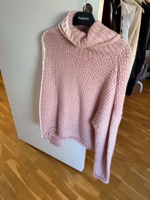 Ljusrosa stickad polotröja  - Mysig ljusrosa stickad polotröja med grovstickad struktur och bred, ribbad polokrage. Tröjan har långa ärmar och avslappnad passform, perfekt för kalla dagar. Materialet känns mjukt och behagligt mot huden.