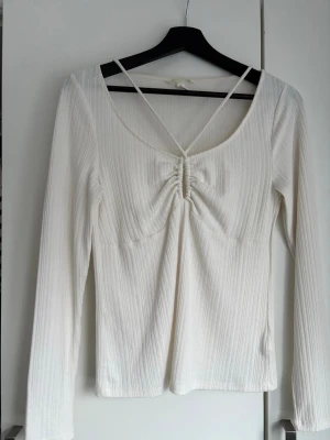 Vit ribbad långärmad topp - Säljer en vit ribbad topp med lång ärm och snygg snörning framtill. Toppen har en djup rundad halsringning med korsade band 