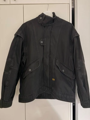 Svart bikerjacka med detaljer - Bikerjacka i denim av G-STAR RAW. Använts en gång. Oversize och unisex. Passar S-L. Ärmarna kan tas av vilket transformerar jackan till en väst! Köpt från Zalando Lounge (kvitto finns)