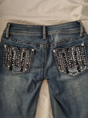2000s jeans med dekorerade fickor - Säljer ett par blå jeans med snygga dekorerade bakfickor med pärlor och paljetter i silver och svart. Jeansen har låg midja, bootcut passform och klassisk femficksdesign. Passar dig som är runt 163-170. Köpte på A2Vintage i mallofscandinavia 2024 för lite mer än 800kr. Säljer pga kommer inte till användning💗💗