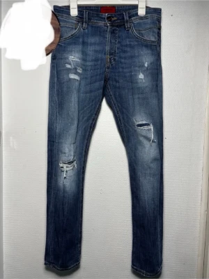 Jack&Jones slim Glenn - Säljer ett par blå ”slim glenn” jeans från Jack&Jones med snygga slitningar och hål på benen. Jeansen har klassisk femficksmodell. Perfekta för en avslappnad och trendig look. W28, L30. Slim Glenn. Bra skick!  