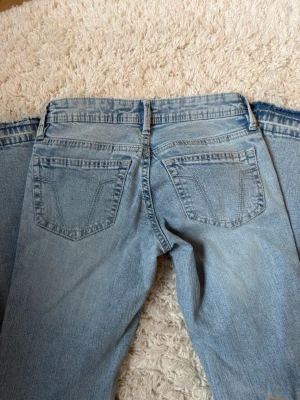 Ljusblå bootcut jeans med utsvängda ben - Säljer ett par ljusblå bootcut jeans med klassiska fem fickor och utsvängda ben. Jeansen har väldigt låg midja och är tillverkade i denim med lätt tvättad look. Perfekta för dig som gillar retrostil och vill ha ett par snygga jeans med 2000-talsvibbar.