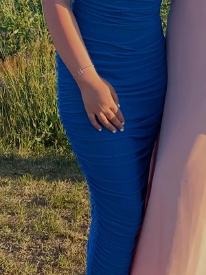 Blå långklänning med åtsittande passform - Snygg blå långklänning med åtsittande siluett och draperade detaljer längs hela klänningen. Perfekt för dig som vill sticka ut med en elegant look. Klänningen har ärmlös design och markerar midjan på ett smickrande sätt.
