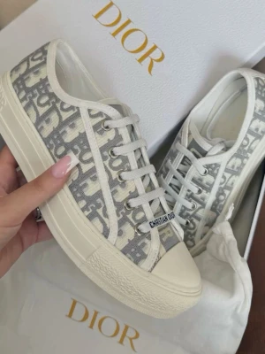 Christian Dior Oblique låga sneakers - Snygga Christian Dior Oblique sneakers i lågt snitt med grått och vitt monogrammönster, som tyvärr inte passar mig. Skorna har vita snören, tåhätta i gummi och robust sula. Klassisk Dior-logga på sidan och canvasmaterial som ger en exklusiv känsla.