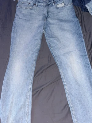 Ljusblå raka jeans från hm - Säljer ett par klassiska ljusblå jeans från hm med rak passform. Jeansen har fem fickor, normal midja och subtila slitningar framtill för en avslappnad look. Tillverkade i slitstark denim som passar perfekt till en trendig vardagsstil.